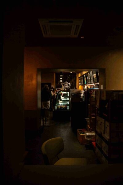 A street photography scene at night featuring a Starbucks café, where the café's interior glow stands out amidst the surrounding urban darkness, capturing the essence of nocturnal city life.