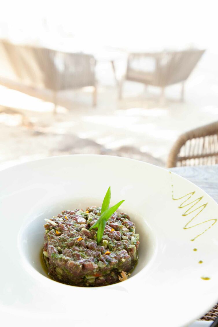 A business photograph of an artfully presented plate of food on a beachfront restaurant in Raiatea, showcasing a delicious dish against the backdrop of the stunning beach.